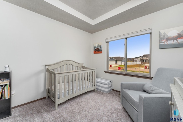 carpeted bedroom featuring a raised ceiling and a nursery area