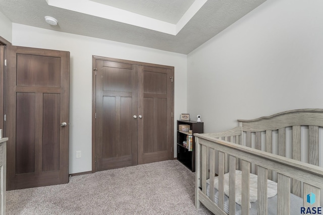 bedroom featuring a textured ceiling, a nursery area, and light carpet