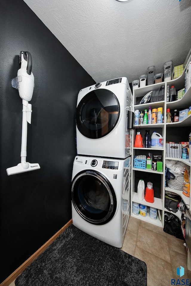 laundry room with a textured ceiling, light tile patterned floors, and stacked washing maching and dryer