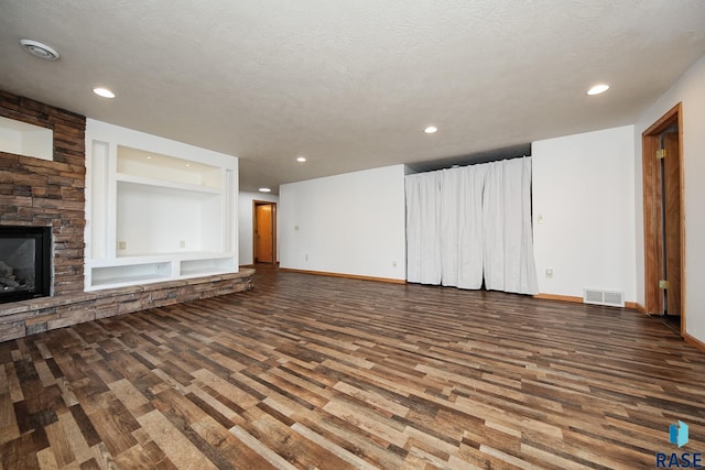 unfurnished living room with hardwood / wood-style floors, built in shelves, a textured ceiling, and a stone fireplace