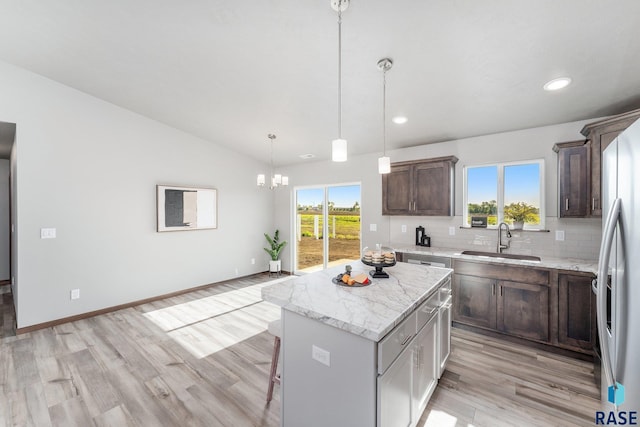 kitchen featuring a center island, light stone countertops, tasteful backsplash, sink, and decorative light fixtures