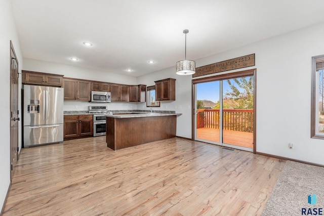 kitchen with hanging light fixtures, light wood-type flooring, sink, kitchen peninsula, and stainless steel appliances