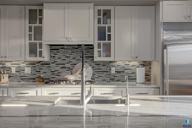 kitchen featuring white cabinets, decorative backsplash, light stone countertops, and stainless steel built in fridge