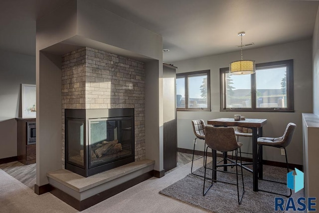 dining space with a multi sided fireplace and light carpet