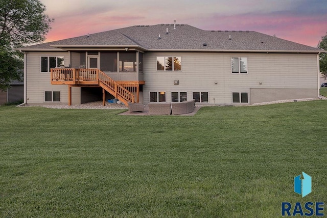 back house at dusk with a wooden deck, a sunroom, and a yard