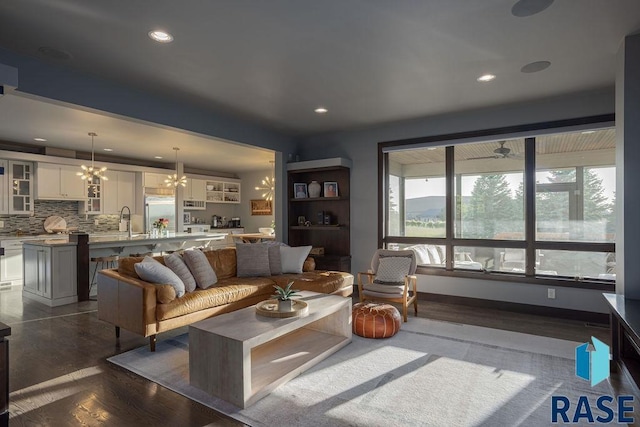 living room with ceiling fan with notable chandelier, sink, and dark wood-type flooring