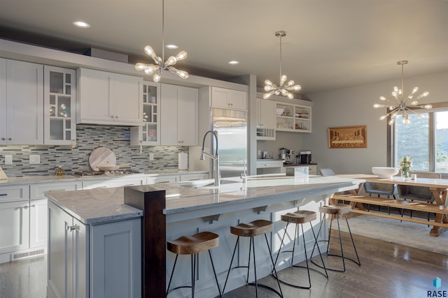 kitchen with a chandelier, a kitchen island with sink, and white cabinets