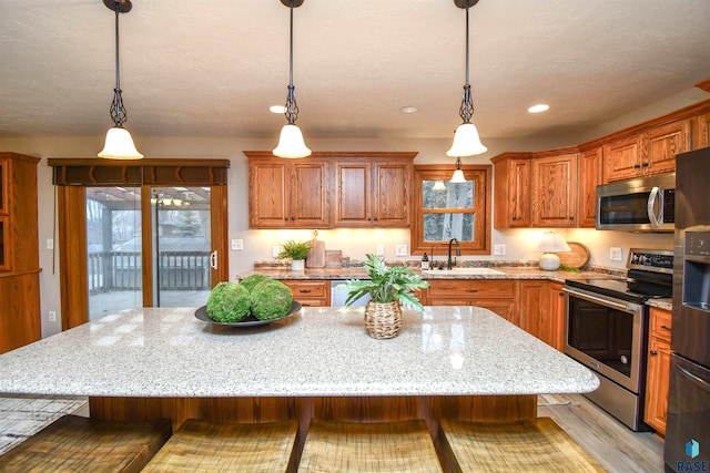 kitchen with sink, hanging light fixtures, appliances with stainless steel finishes, and a kitchen breakfast bar