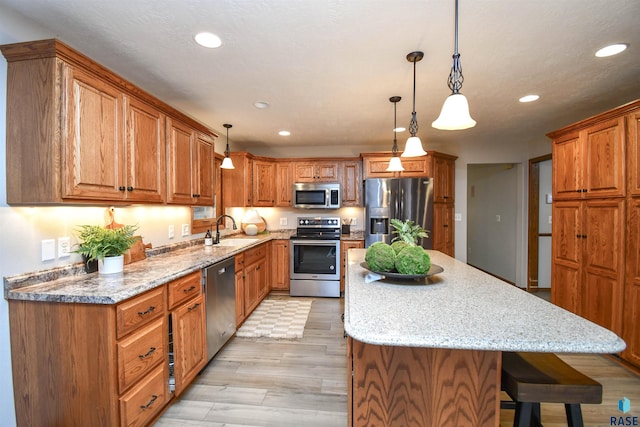 kitchen with light hardwood / wood-style flooring, sink, decorative light fixtures, a kitchen bar, and stainless steel appliances