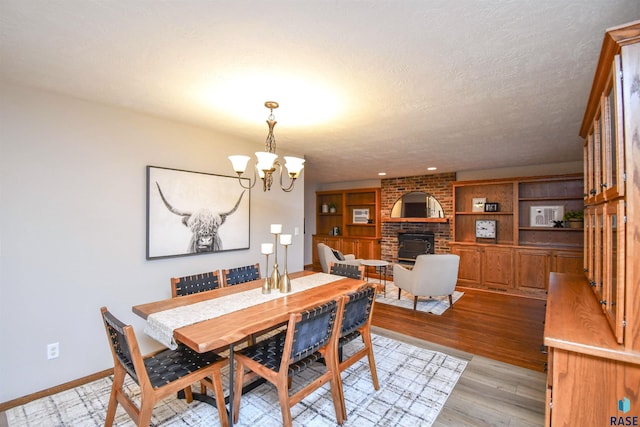 dining area featuring a fireplace, a chandelier, light hardwood / wood-style flooring, and a textured ceiling