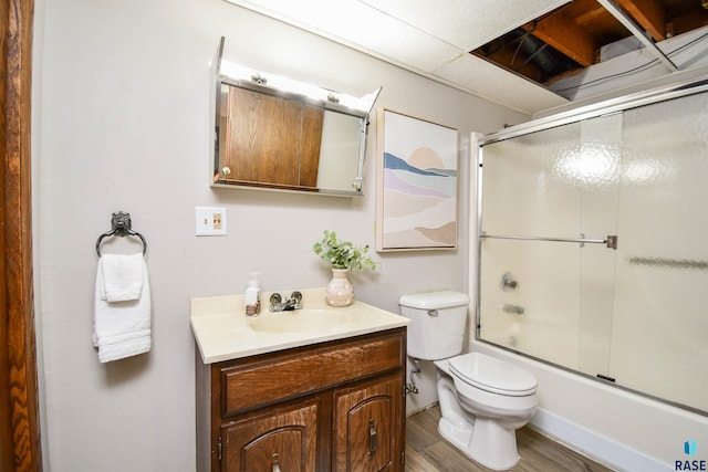 full bathroom with vanity, hardwood / wood-style flooring, bath / shower combo with glass door, and toilet