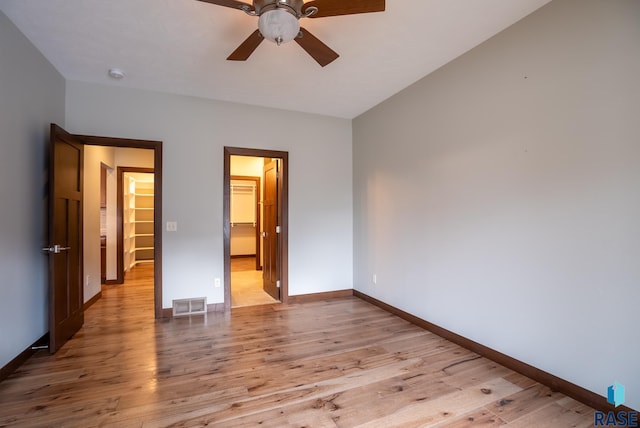 unfurnished bedroom with light hardwood / wood-style floors, a closet, a walk in closet, and ceiling fan