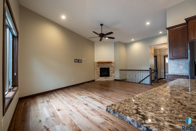 unfurnished living room featuring ceiling fan, light hardwood / wood-style floors, and a stone fireplace