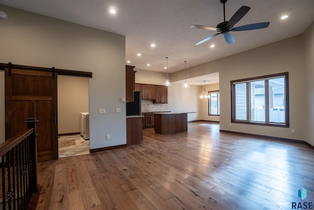 kitchen with pendant lighting, hardwood / wood-style floors, a center island, black refrigerator, and a barn door