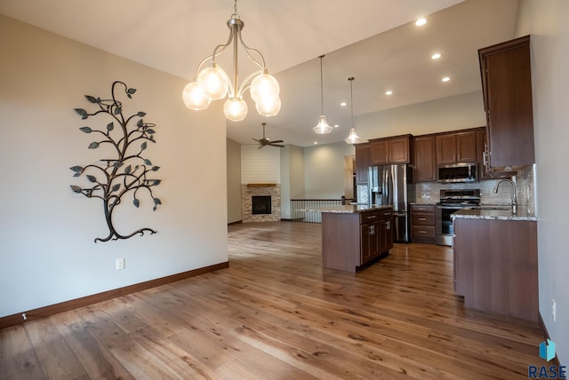 kitchen with appliances with stainless steel finishes, a kitchen island, decorative light fixtures, sink, and light stone counters