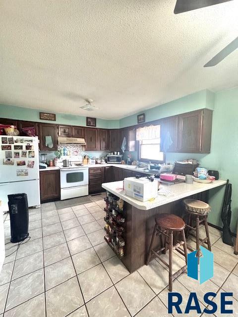 kitchen with dark brown cabinets, white appliances, kitchen peninsula, and a kitchen bar