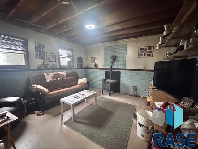 living room featuring a wood stove, brick wall, and concrete flooring