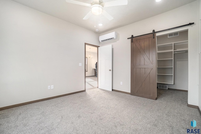 unfurnished bedroom featuring ceiling fan, a closet, a wall unit AC, light colored carpet, and a barn door