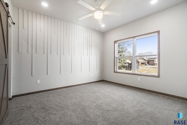 empty room featuring a barn door, ceiling fan, and carpet flooring