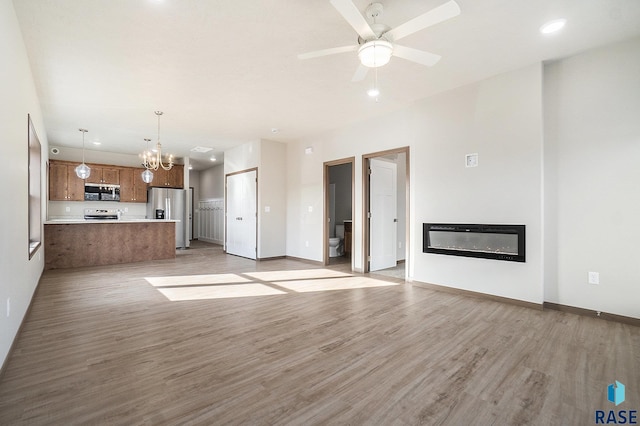 unfurnished living room with ceiling fan with notable chandelier and light wood-type flooring