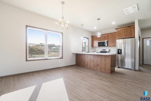 kitchen featuring pendant lighting, stainless steel appliances, a chandelier, and light wood-type flooring