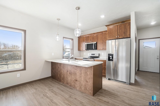 kitchen featuring sink, hanging light fixtures, kitchen peninsula, stainless steel appliances, and light hardwood / wood-style floors