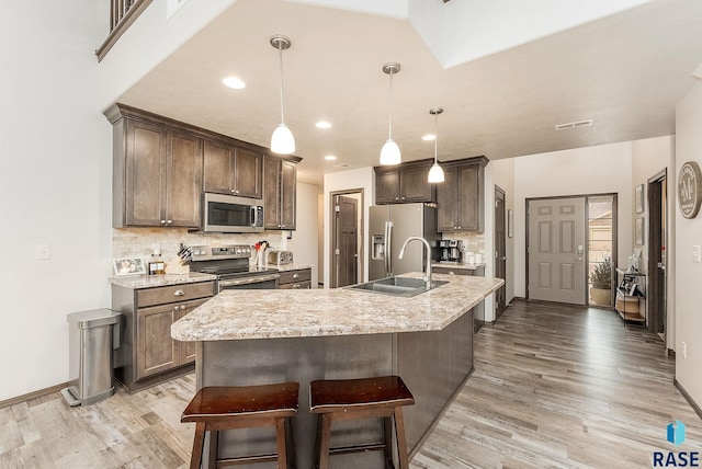 kitchen featuring dark brown cabinets, appliances with stainless steel finishes, sink, decorative light fixtures, and an island with sink