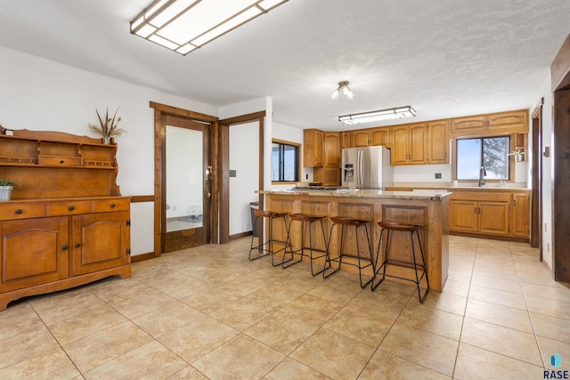 kitchen with appliances with stainless steel finishes, a kitchen island, a kitchen breakfast bar, sink, and light tile patterned floors