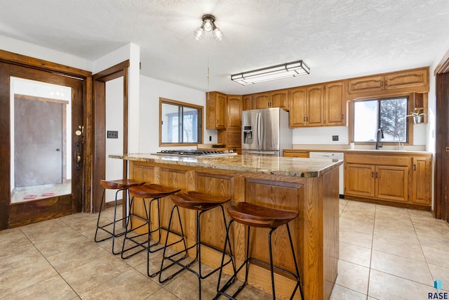 kitchen with appliances with stainless steel finishes, a textured ceiling, a kitchen breakfast bar, sink, and a kitchen island