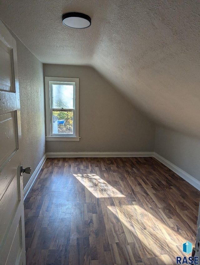 additional living space featuring dark wood-type flooring, a textured ceiling, and lofted ceiling