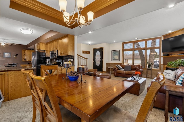 dining area with ceiling fan with notable chandelier and a raised ceiling