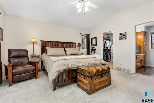 carpeted bedroom with ensuite bath, lofted ceiling, a walk in closet, a closet, and ceiling fan