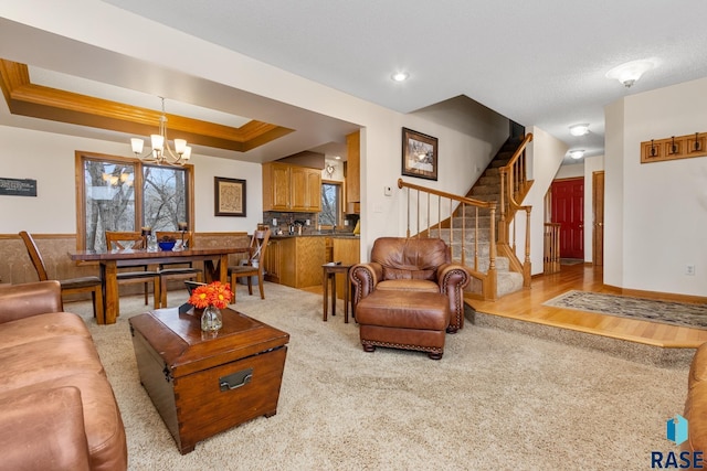 carpeted living room with a tray ceiling, ornamental molding, and an inviting chandelier