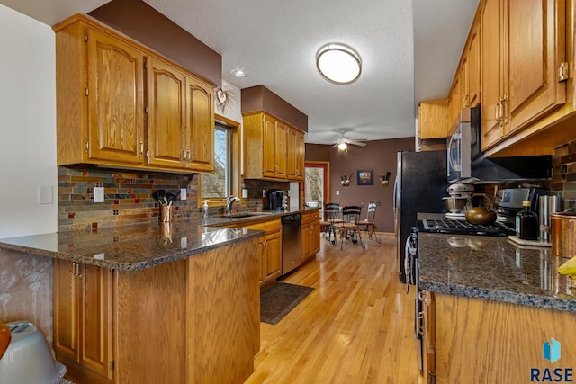 kitchen with light hardwood / wood-style floors, dark stone counters, sink, kitchen peninsula, and stainless steel appliances