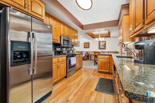 kitchen with dark stone counters, sink, a raised ceiling, light hardwood / wood-style flooring, and stainless steel appliances