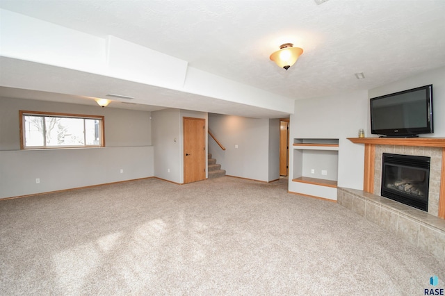 unfurnished living room with carpet, built in shelves, a tile fireplace, and a textured ceiling