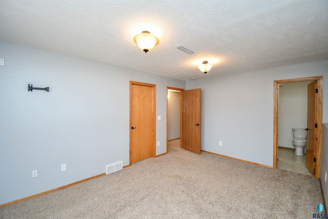 unfurnished bedroom featuring a closet, a textured ceiling, light carpet, and ensuite bath