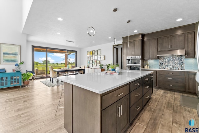 kitchen featuring dark brown cabinetry, a center island, light hardwood / wood-style floors, backsplash, and hanging light fixtures