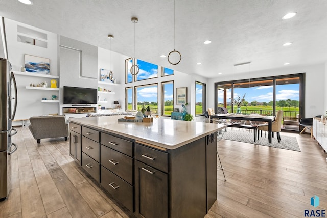 kitchen with dark brown cabinetry, a kitchen island, decorative light fixtures, stainless steel fridge, and light hardwood / wood-style flooring