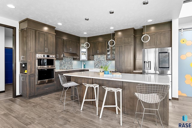 kitchen with a center island, appliances with stainless steel finishes, tasteful backsplash, a barn door, and light hardwood / wood-style flooring