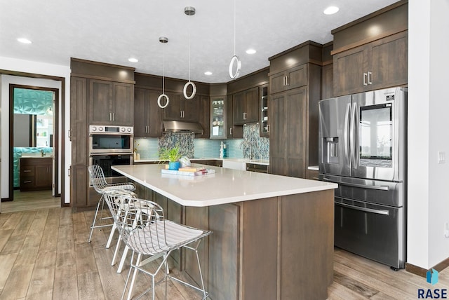 kitchen with a kitchen island, decorative light fixtures, stainless steel appliances, a breakfast bar, and light hardwood / wood-style flooring