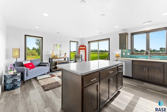 kitchen with a kitchen island, sink, backsplash, stainless steel dishwasher, and light hardwood / wood-style flooring