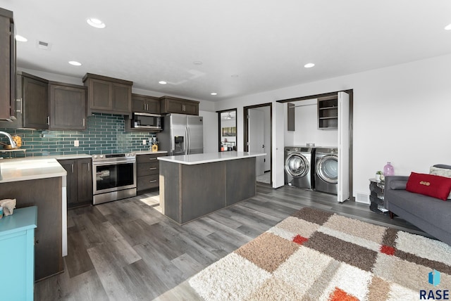 kitchen with washing machine and clothes dryer, decorative backsplash, a kitchen island, dark brown cabinetry, and stainless steel appliances