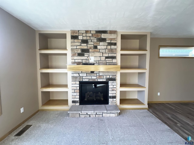 unfurnished living room with carpet floors, built in shelves, a textured ceiling, and a stone fireplace