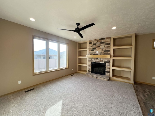 unfurnished living room featuring ceiling fan, built in features, carpet, a fireplace, and a textured ceiling