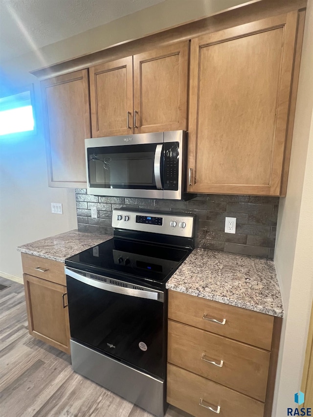 kitchen with light wood-type flooring, stainless steel appliances, light stone counters, and backsplash