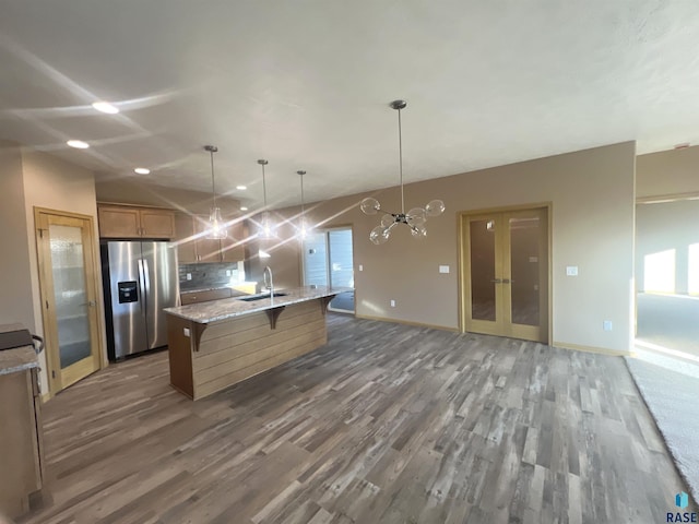 kitchen featuring stainless steel fridge, dark hardwood / wood-style flooring, sink, decorative light fixtures, and an island with sink