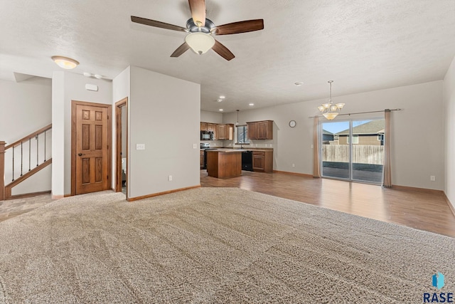 unfurnished living room with ceiling fan with notable chandelier and light carpet