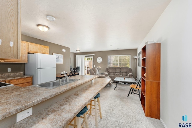 kitchen with sink, a kitchen breakfast bar, white refrigerator, a textured ceiling, and light carpet