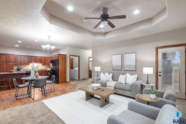 living room featuring a raised ceiling, separate washer and dryer, ceiling fan with notable chandelier, and light wood-type flooring